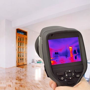 Handheld thermal camera scanning a room for heat patterns.