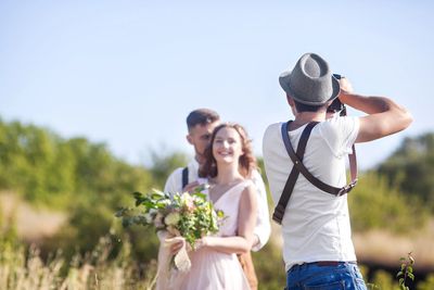 A photographer captures a smiling couple in a sunlit outdoor setting.