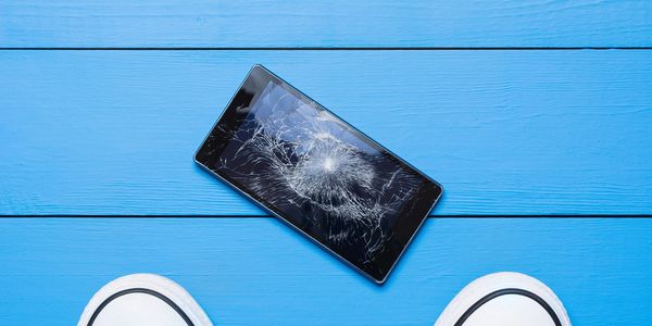 Cracked smartphone screen on blue floor with shoes nearby.