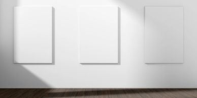 Three blank white canvases hang on a wall with sunlight.