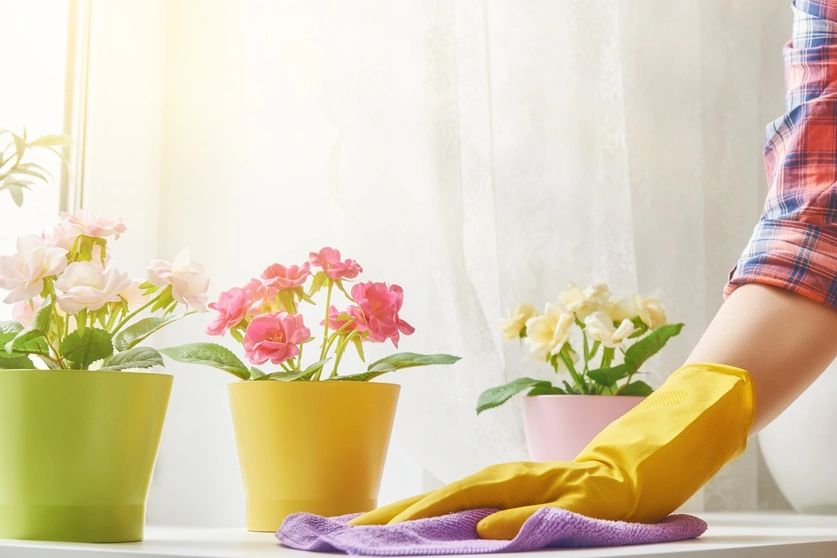 Person cleaning a white table with yellow gloves and a spray bottle.
