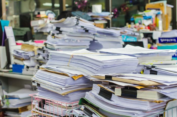 Stacks of documents and papers piled high on office desks.