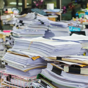 Stacks of organized and disorganized paper documents piled high on desks.