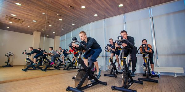 Group cycling class in a modern gym with wooden ceiling and large mirrors.