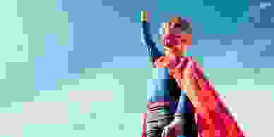 A child wearing a superman suit with his fist clenched and raised in the air.