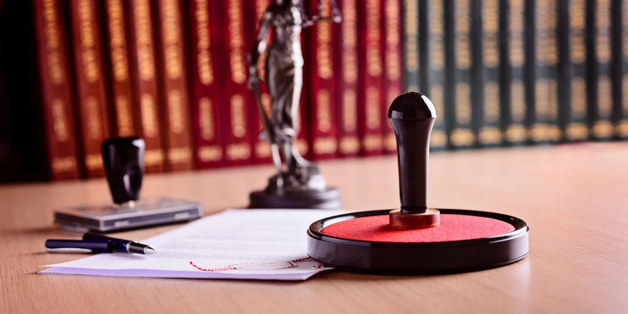A large red ink stamp on a desk with legal books and documents in the background.