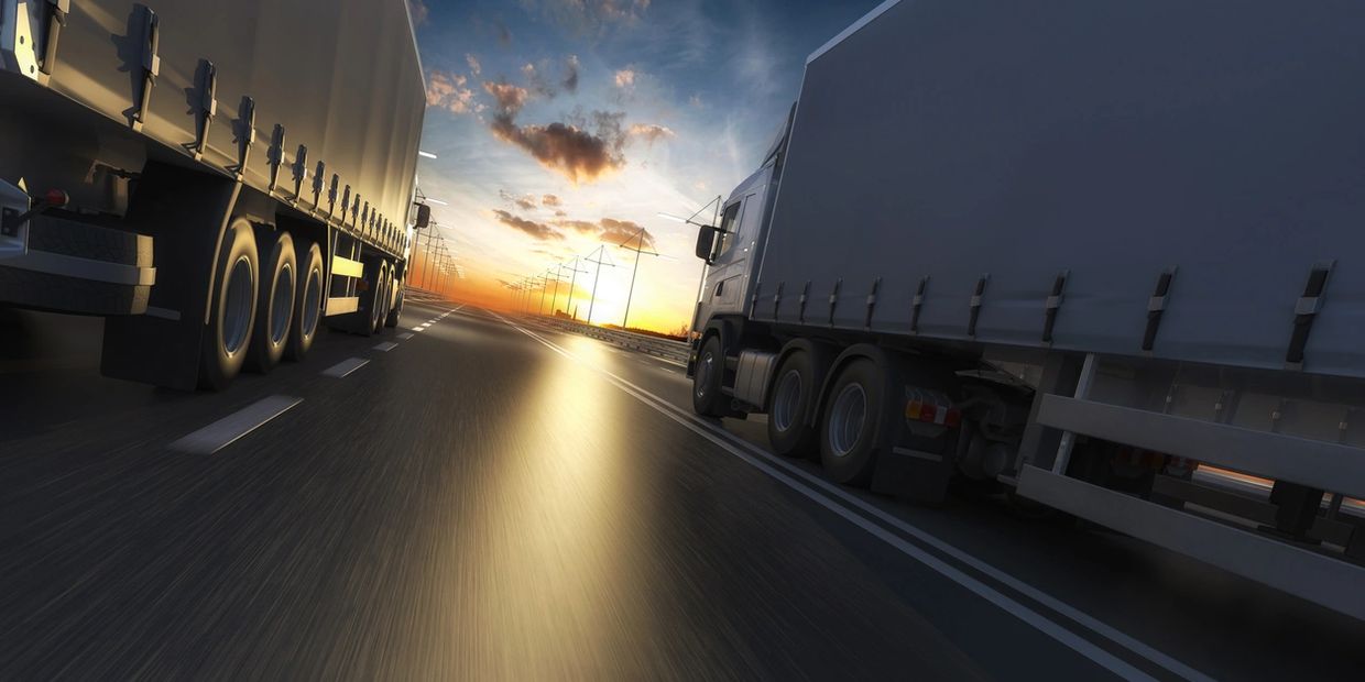 A dynamic shot of two semi trucks passing each other on the highway during an orange sunset