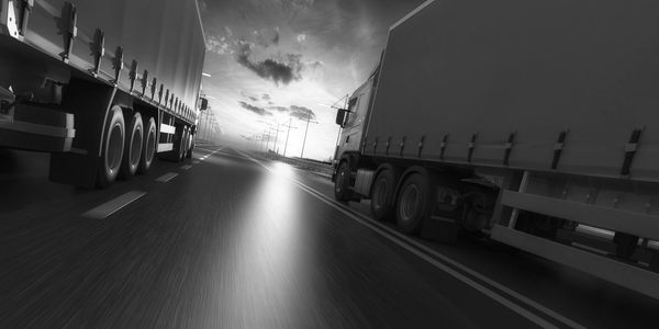 Two large trucks driving side by side on a highway at sunset.
