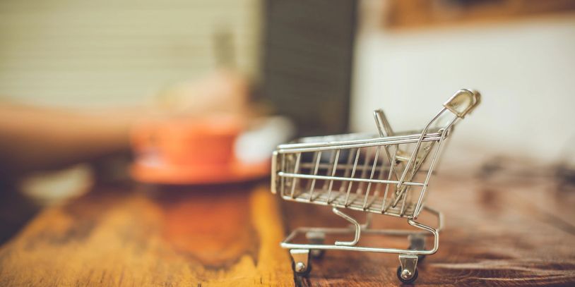 Tiny shopping cart on a wooden table with blurred background.