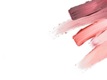 Three brush strokes of pink and red paint on a white background.