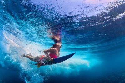 Surfer underwater with surfboard surrounded by blue waves.