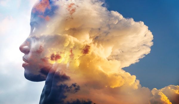 Profile of a person blended with a dramatic cloudscape at sunset.