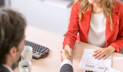Two professionals shaking hands over a desk with documents and coffee cups.