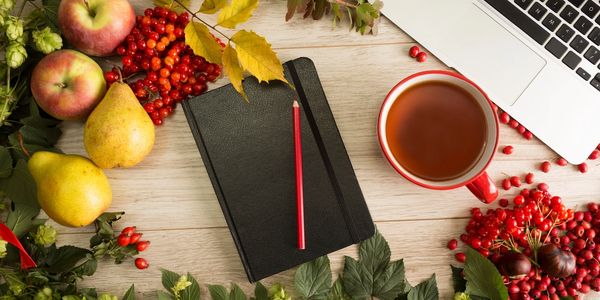Autumn workspace with fruits, berries, notebook, tea, and laptop on wooden table.