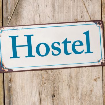 Signboard with "Hostel" text hanging on a wooden door.