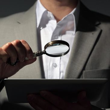 man holding magnifying glass to look at data on laptop screen