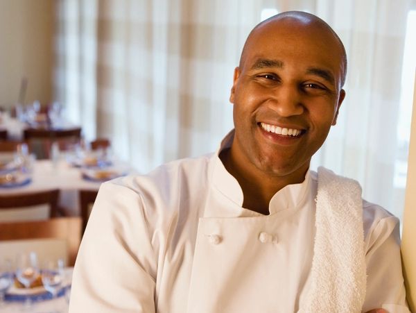 Smiling chef in a white uniform standing in a restaurant.