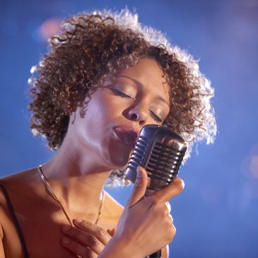 A woman passionately singing into a vintage microphone under soft lighting.