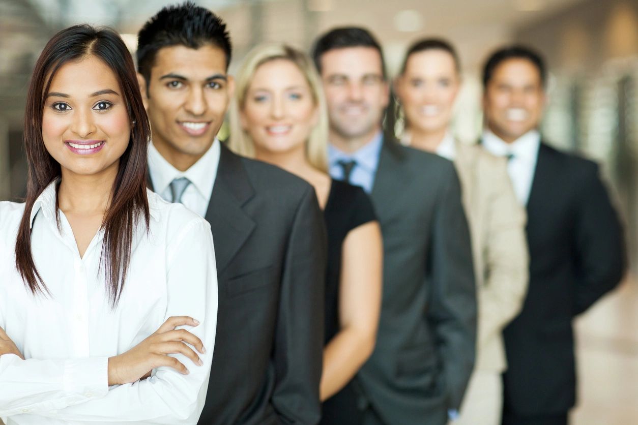 A group of professionally dressed people are in a single file line, looking ahead and smiling.