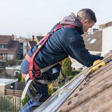 Worker installing solar panels on a roof with safety harness.