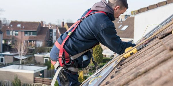 Worker in safety harness repairing a roof with tools.