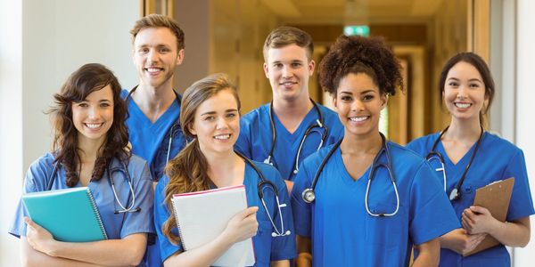 Group of smiling medical students in blue scrubs with stethoscopes and notebooks.