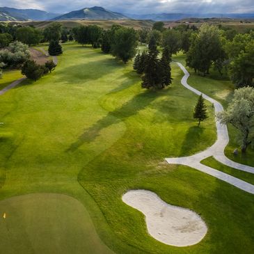 A sunny golf course with green grass, sand bunkers, and a winding path.