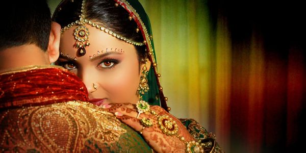 Bride in traditional attire embracing groom with intense eyes and intricate jewelry.