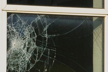 Broken window glass with a spiderweb-like crack pattern.