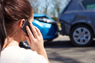 A woman stands before a two car accident, using a cell phone to call workers' compensation lawyer