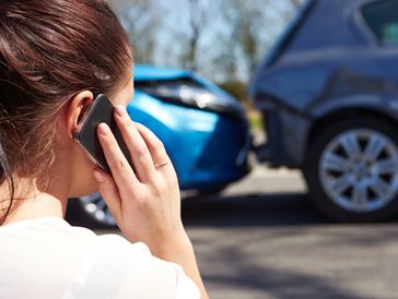 Woman on phone after a car accident with damaged vehicles.