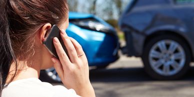 Lady speaking into a cell phone while looking at two cars that have collided with each other 