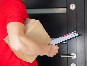 Delivery person holding a package and clipboard at a door.