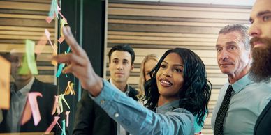 Employees standing and pointing at sticky notes in a meeting