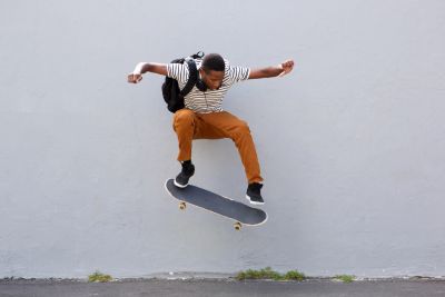 Young man performing a skateboard trick in mid-air against a plain wall.