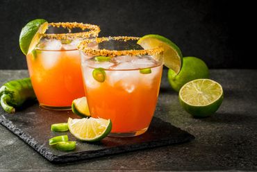 Two spicy orange cocktails garnished with lime and chili slices.