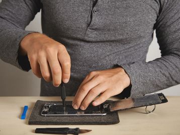 Person repairing a smartphone using a screwdriver on a work mat.