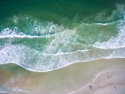 Aerial view of ocean waves gently crashing on a sandy beach.
