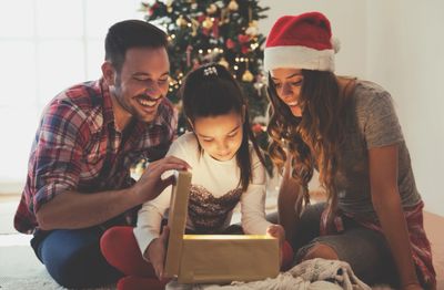 A family with a young school-aged child opening a gift in front of a holiday tree