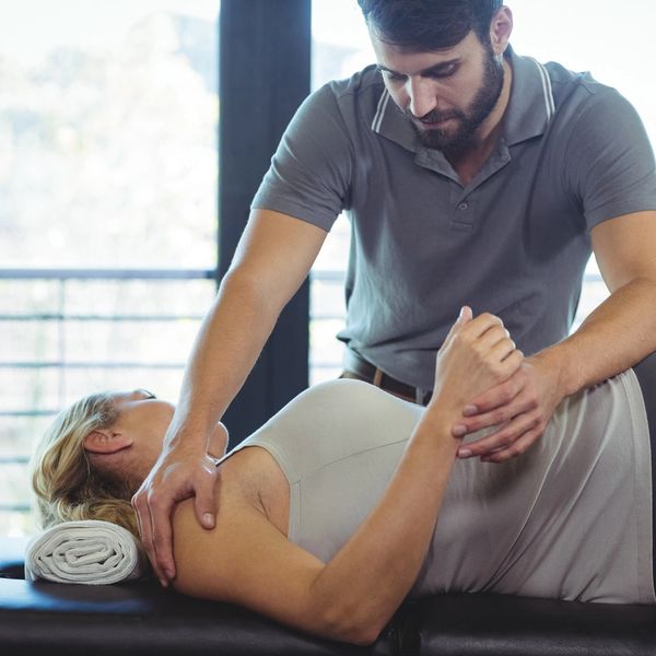 Therapist assisting woman with shoulder and arm stretch on therapy table.