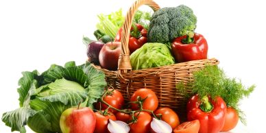 A basket filled with fresh vegetables and fruits including broccoli, tomatoes, and apples.