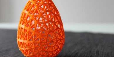 3D Printing Service Print in Orange ASA Filament in a Egg Design placed on a grey floor. 