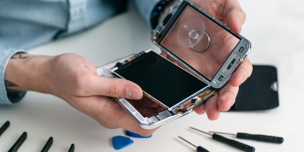 Hands repairing a disassembled smartphone with tools on the table.