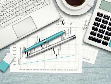 Workspace with laptop, calculator, pens, and financial chart.