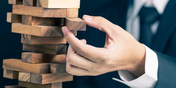 A man’s hand is pulling a piece out of a Jenga block.