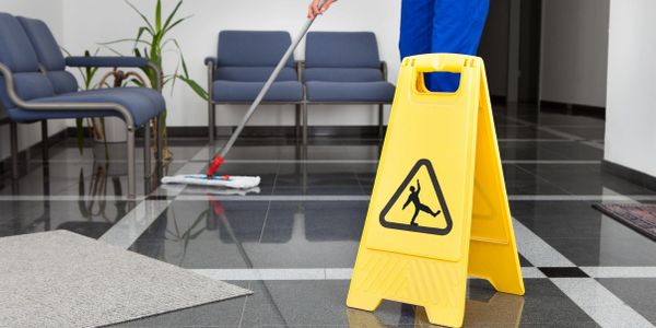 Shows a cleaner who is cleaning a office floor showing yellow cleaning sign. 