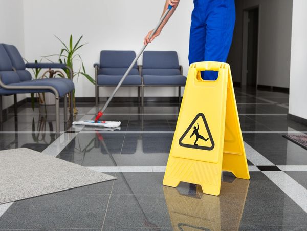 Yellow wet floor sign with person mopping floor in background.