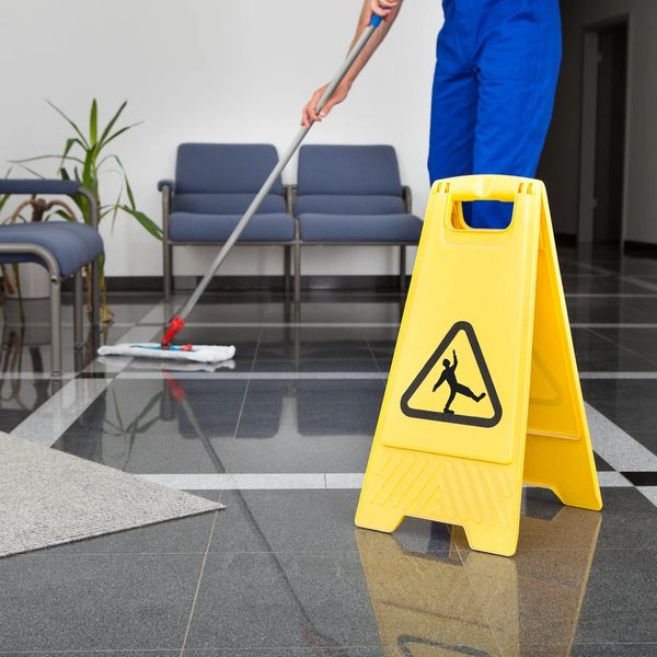 Yellow caution sign on wet floor with person mopping in background.