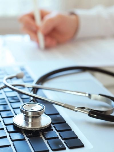 Stethoscope on laptop keyboard with a person writing in the background.