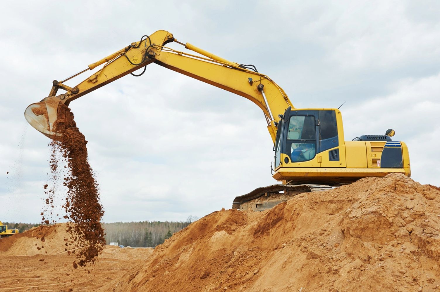 Yellow excavator dumping soil at a construction site.